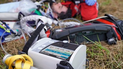 Un respirateur de WEINMANN est posé sur une prairie au premier plan. Des secouristes s'occupent d'une personne blessée.