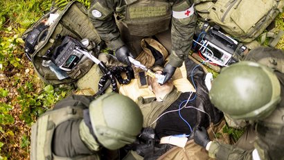 Soldaten leisten in einem Waldgebiet Erste Hilfe bei einer verletzten Person. Beatmungs- und Überwachungsgeräte sind im Einsatz.