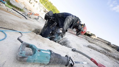 A member of the I.S.A.R. Germany rescue team, wearing protective clothing, is working with a hammer drill