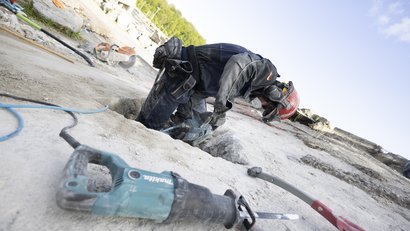 A member of the I.S.A.R. Germany rescue team, wearing protective clothing, is working with a hammer drill