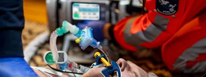 Eine verletzte Person liegt auf dem Boden und wird künstlich beatmet. Ein Rettungsteam nutzt ein Beatmungsgerät, um die Person zu versorgen.