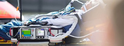 Un patient est allongé sur un brancard et est équipé d'un respirateur de WEINMANN. L'appareil affiche les signes vitaux et les paramètres de ventilation.