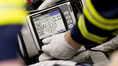 Deux secouristes transportent une personne blessée sur une civière jusqu'à l'ambulance. La personne est reliée à des appareils médicaux et reçoit de l'oxygène.