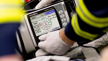 Deux secouristes transportent une personne blessée sur une civière jusqu'à l'ambulance. La personne est reliée à des appareils médicaux et reçoit de l'oxygène.