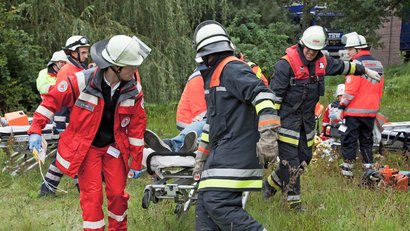 Zwei Helfer vom Roten Kreuz versorgen eine Person mit einer goldenen Rettungsdecke. Sie sind in einem Zelt mit vielen medizinischen Geräten.