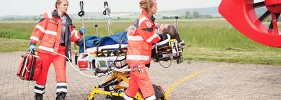 Emergency paramedics transport a patient with a ventilator on a stretcher to the rescue helicopter.