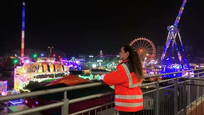 Eine Frau in roter Einsatzkleidung blickt von einer erhöhten Plattform auf den Hamburger Dom bei Nacht.