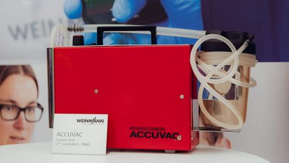 The second generation ACCUVAC suction pump is displayed in a red housing with a connected secretion container.
